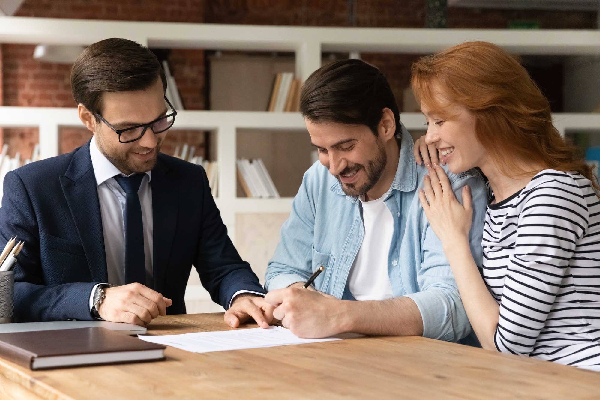 Excited young Caucasian couple sign contract make deal buy house at male relator or broker.